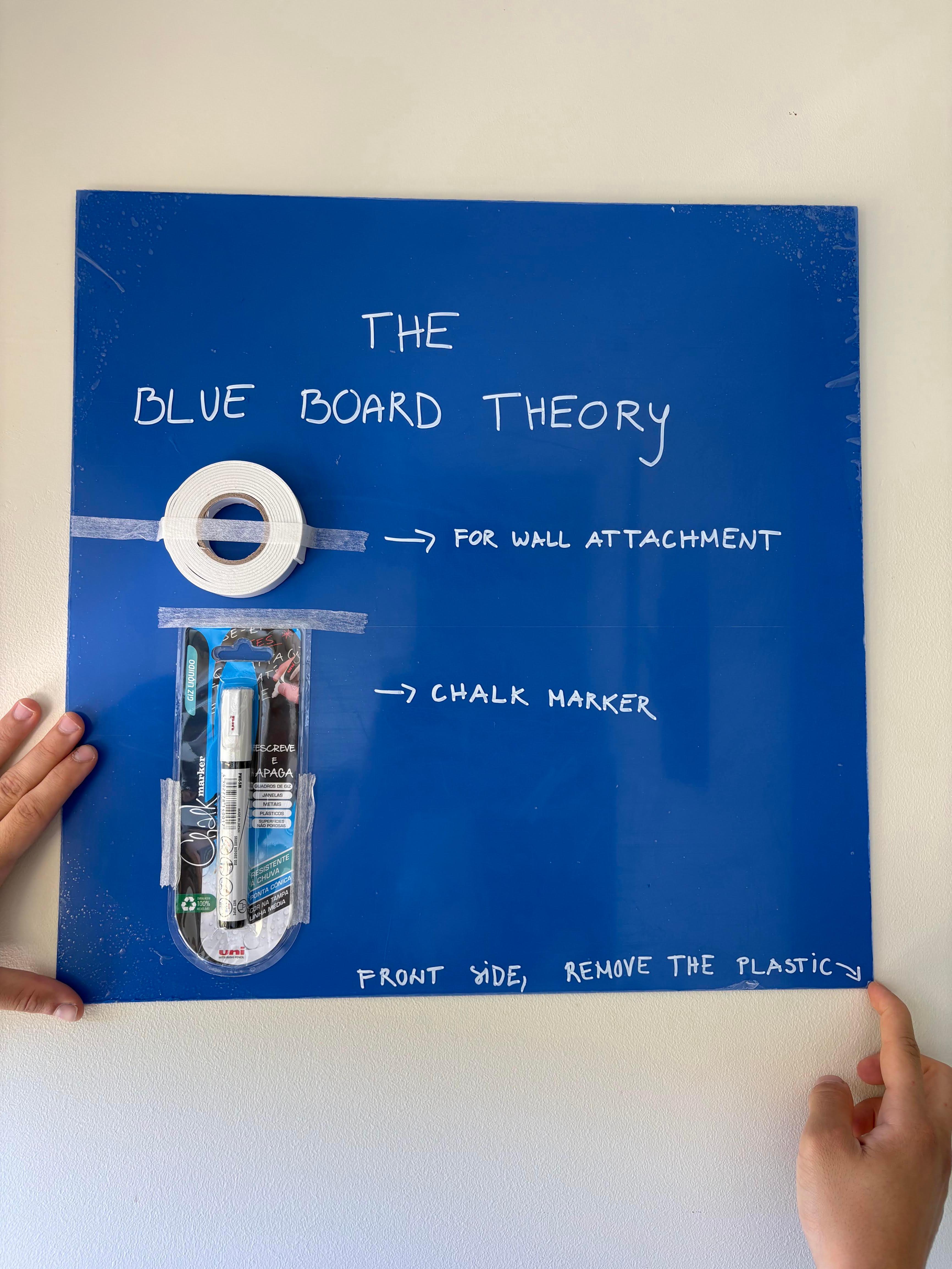 The board held to a wall, showing the included mounting tape and white chalk marker, with the front protective film ready to peel.